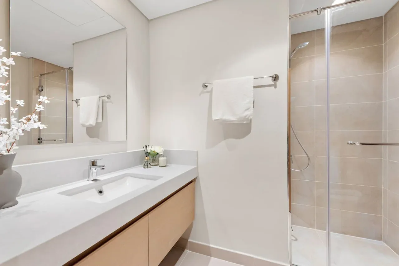Un baño luminoso con lavabo, mueble de baño y ducha con mampara de vidrio.