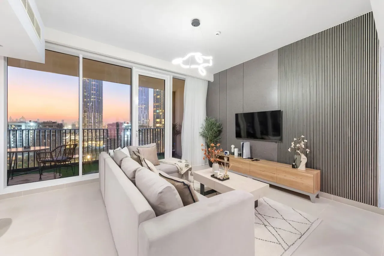A modern living room with a sofa facing a television and a balcony view.