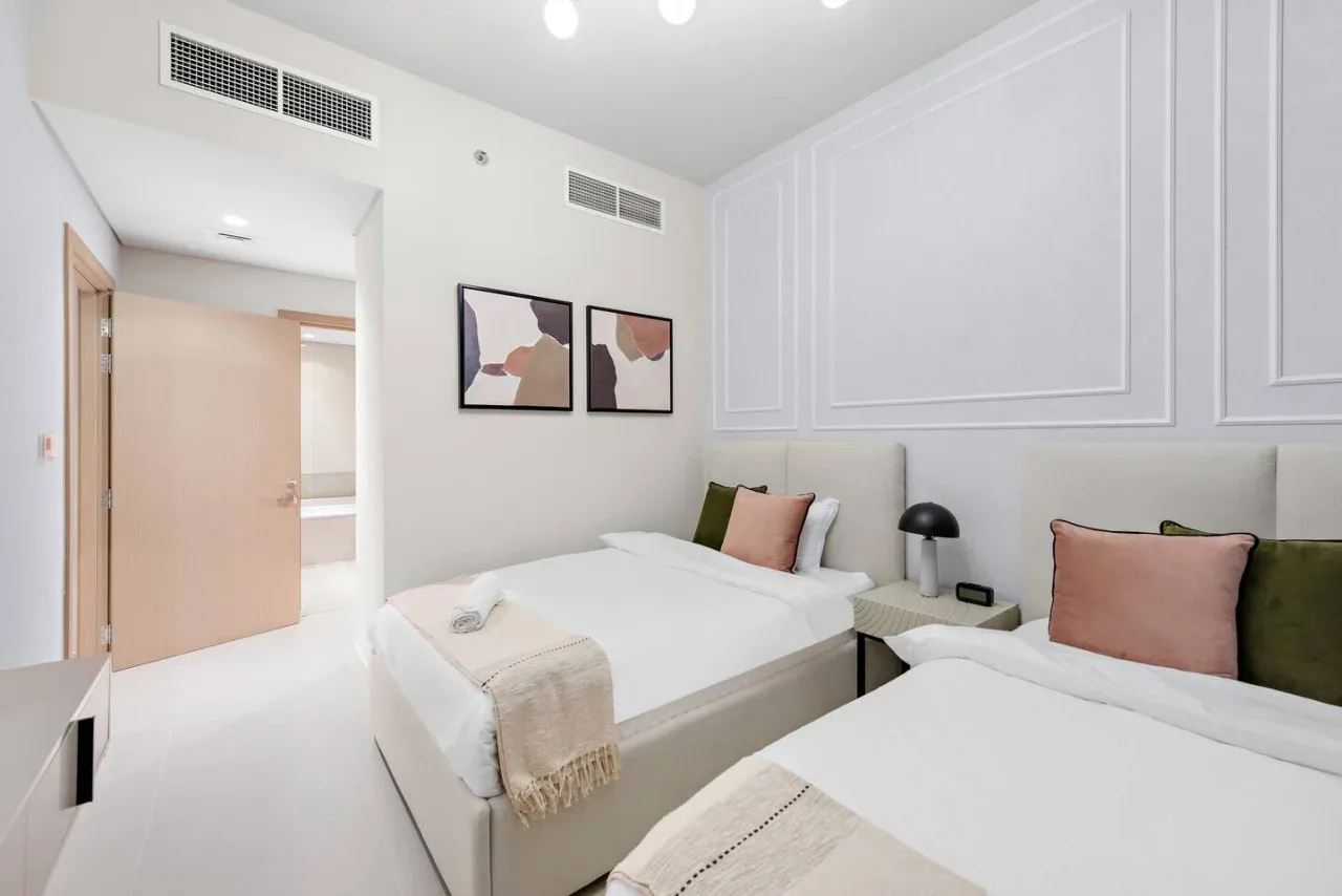 Un dormitorio luminoso con dos camas, ropa de cama blanca y cuadros enmarcados.