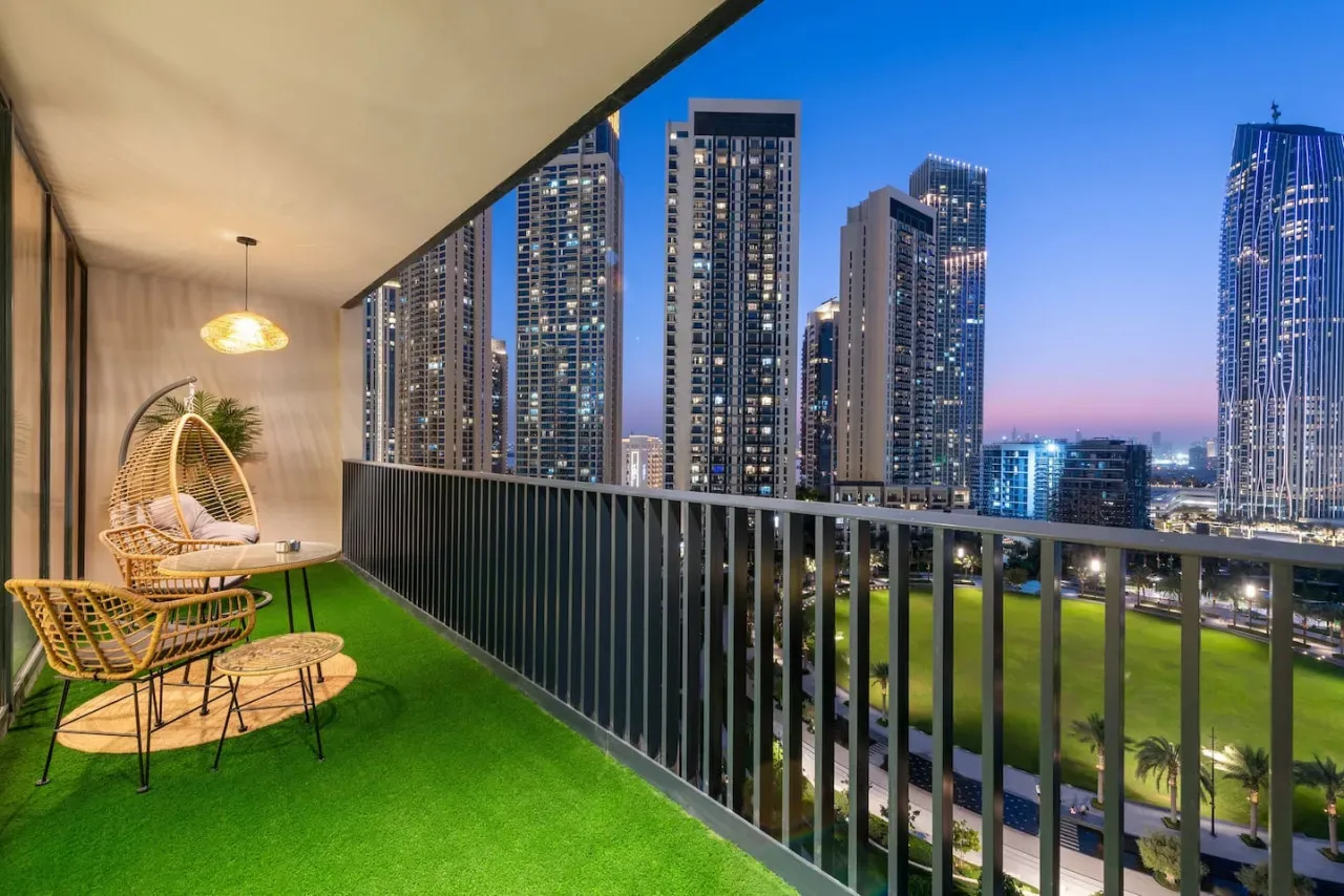 A balcony seating area overlooks illuminated high-rise buildings at dusk.