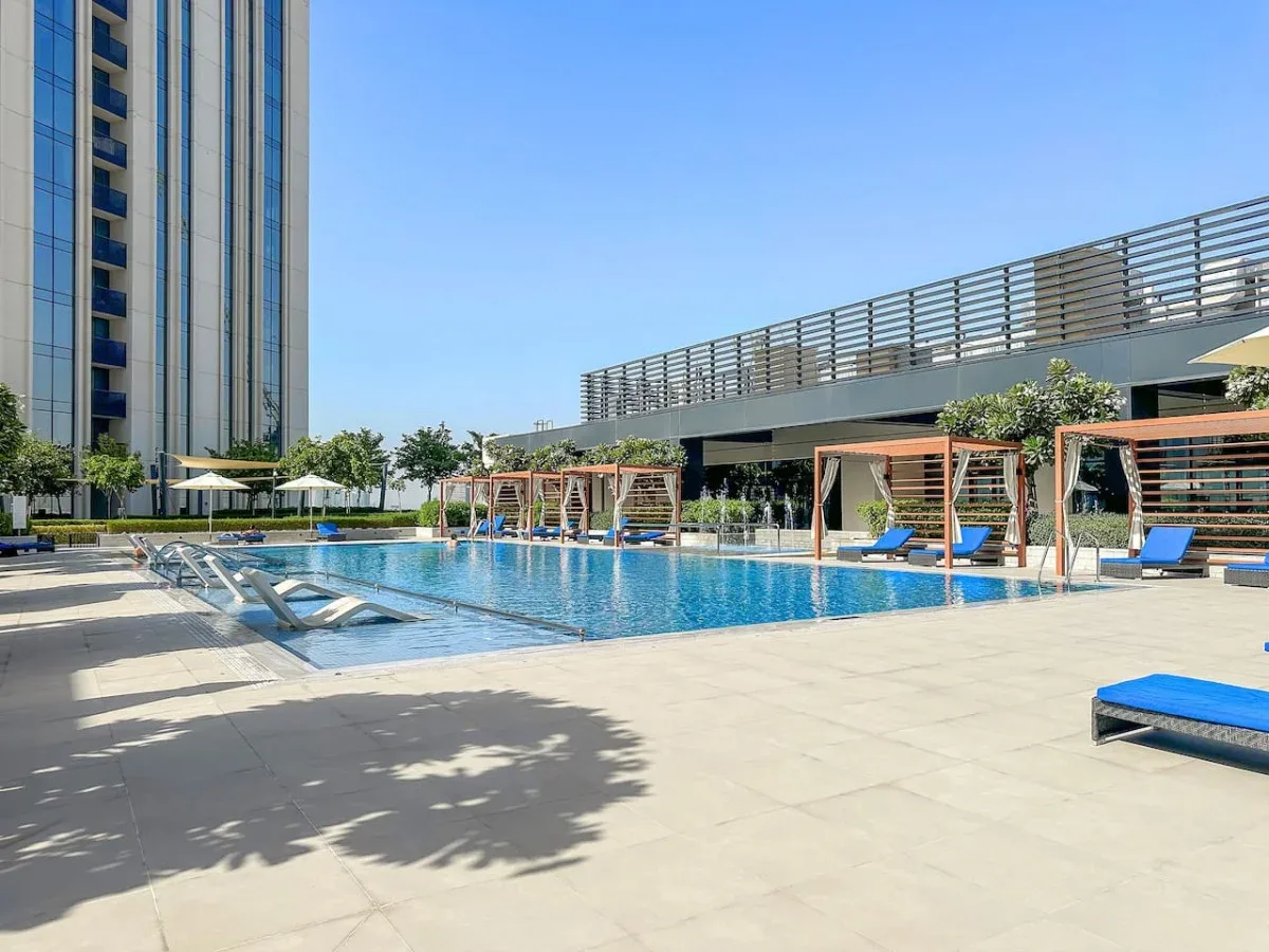 Una piscina al aire libre está junto a un edificio moderno, con asientos para descansar en la terraza.