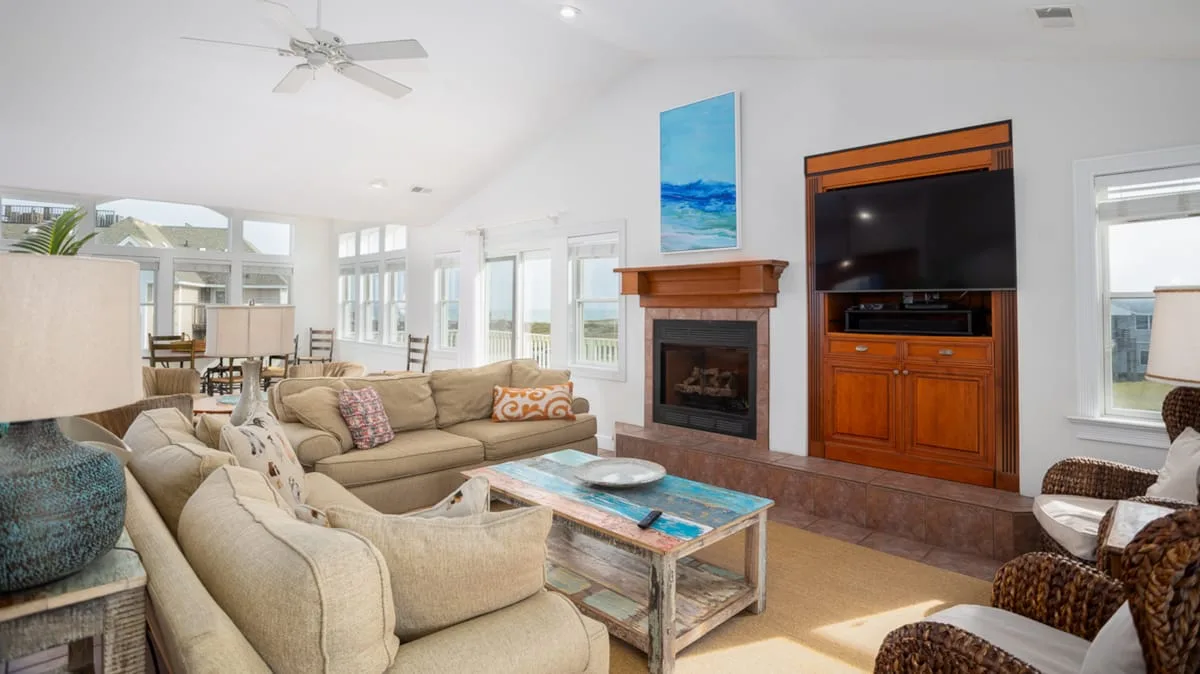 A bright living room with seating arranged around a fireplace and television.