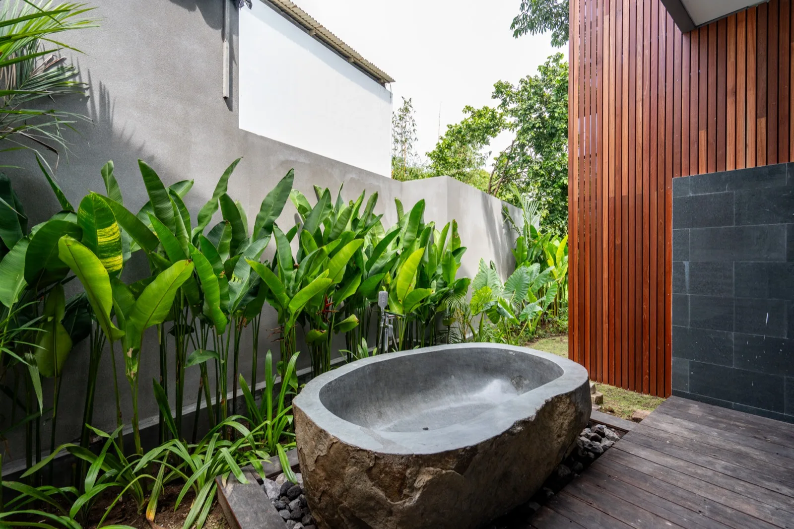 Una bañera exterior está junto a plantas frondosas y una terraza de madera.