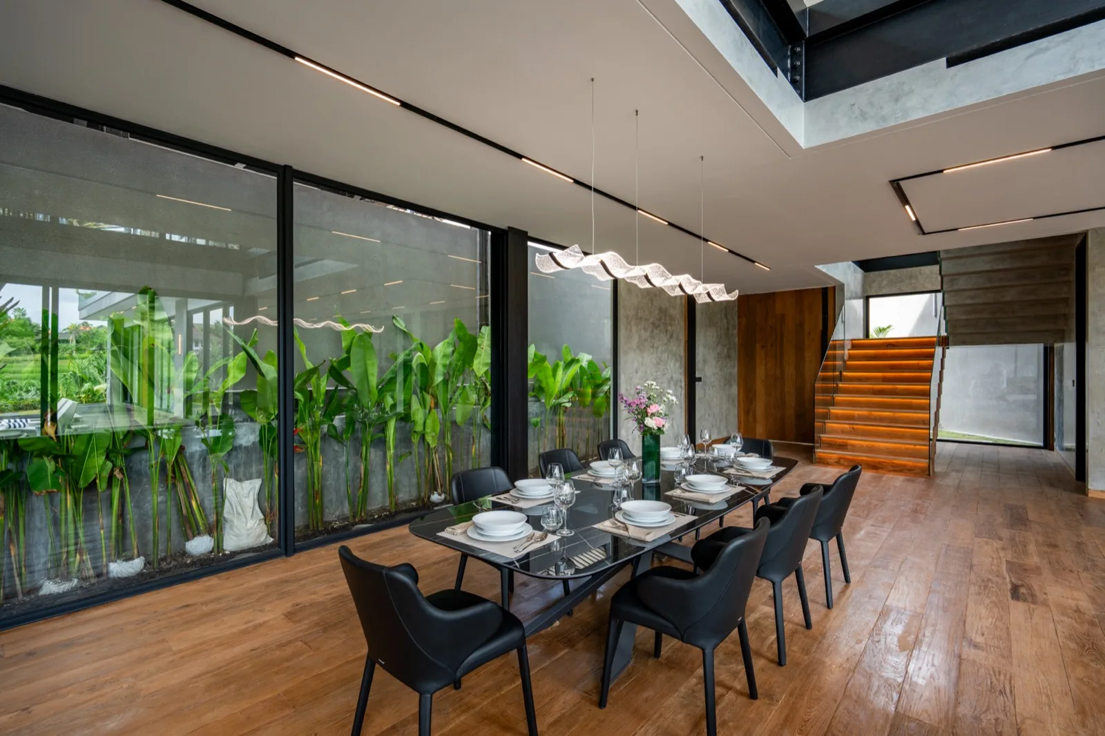 A dining area with a long table and dark seating beside large windows.