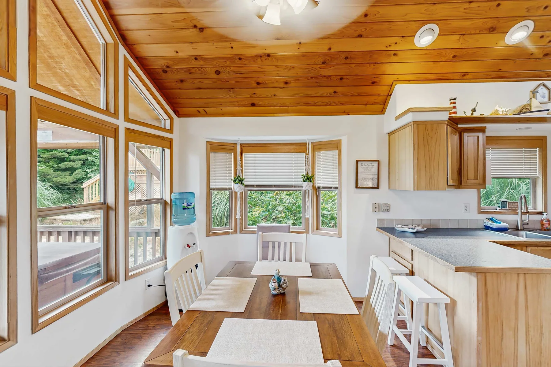 Un comedor luminoso con grandes ventanas, una mesa de madera y una encimera de cocina.