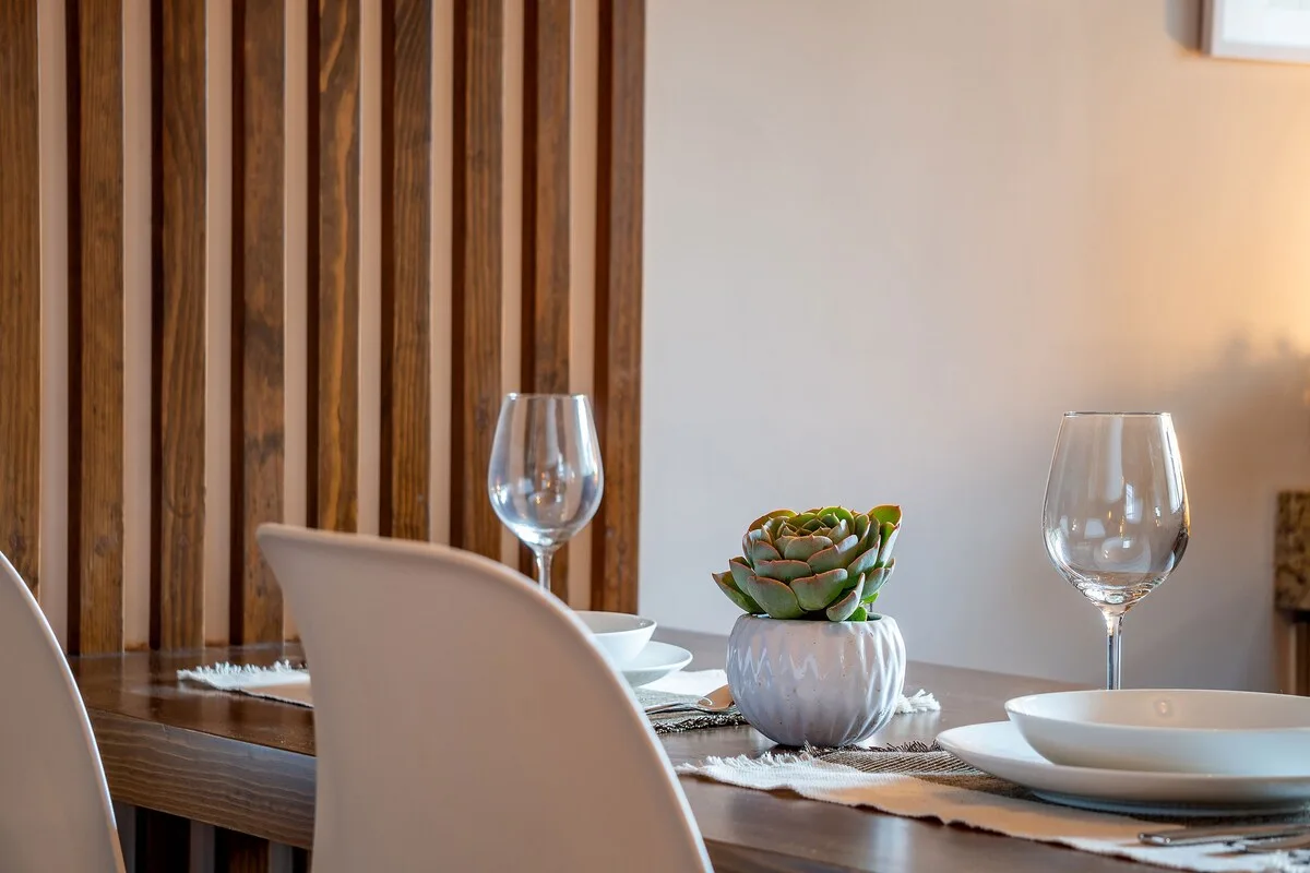 A dining table is set with dishes, wine glasses, and a small potted succulent.