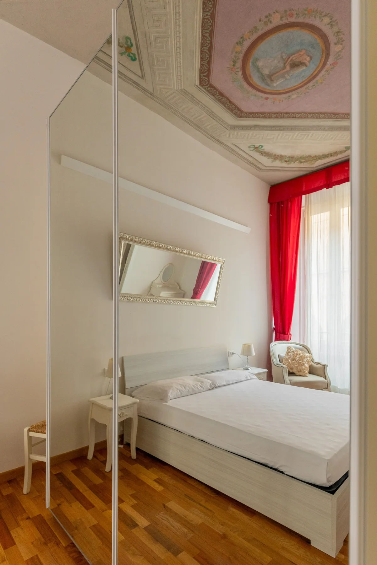 Un dormitorio con cama, armario con espejo y cortinas rojas junto a la ventana.