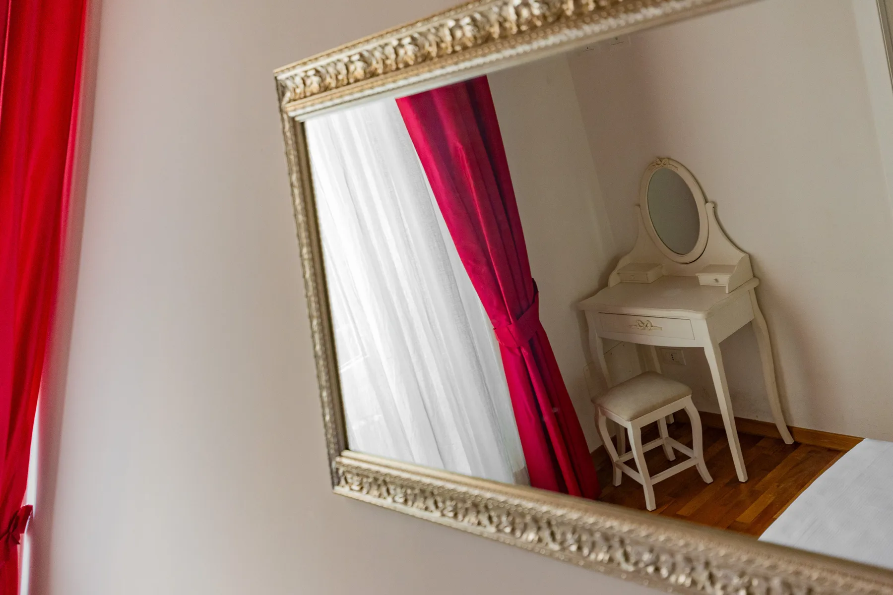 Un espejo refleja un tocador y un taburete junto a cortinas rojas y blancas.