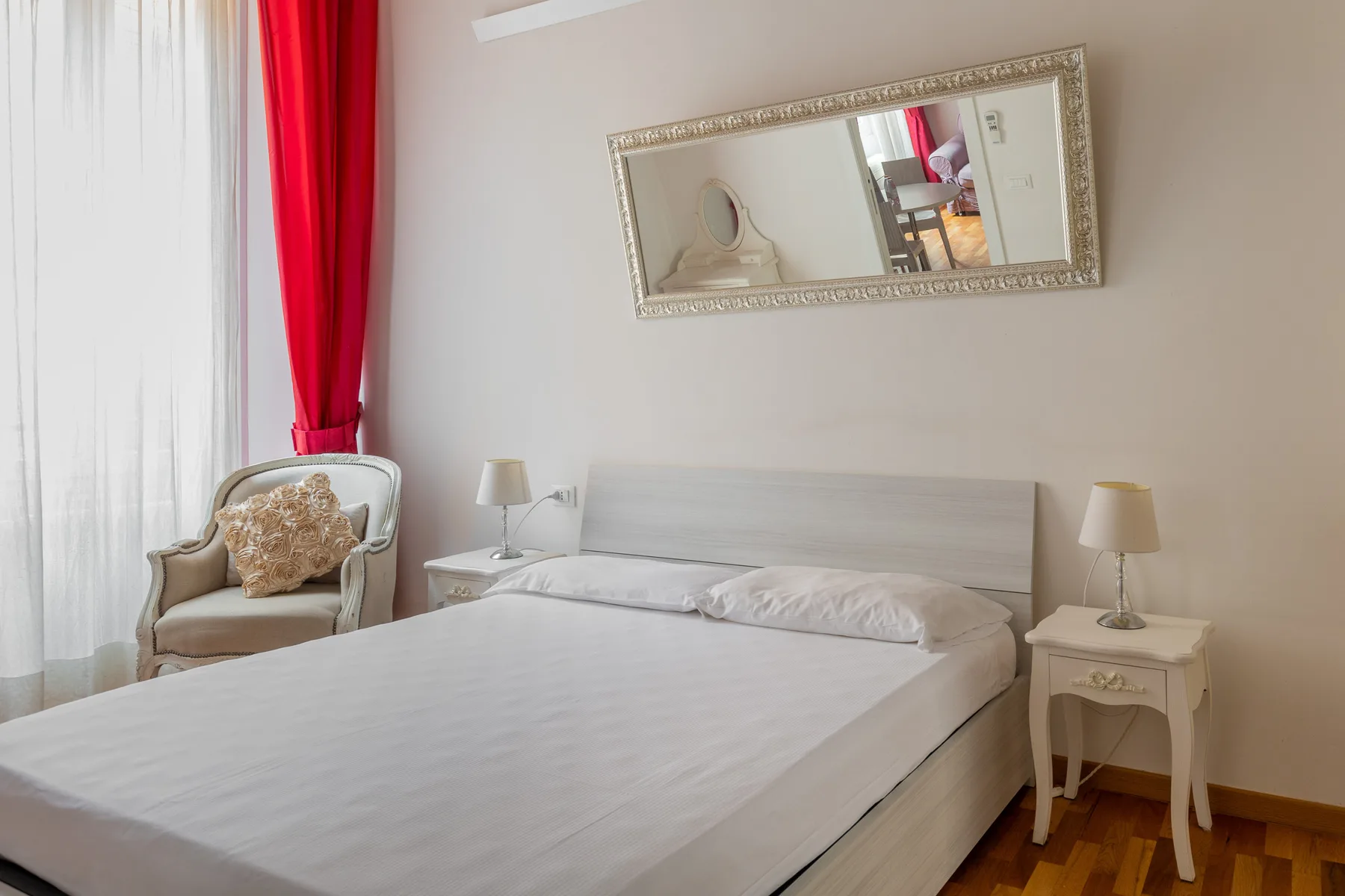 Un dormitorio con una cama bien tendida, mesitas de noche y un espejo enmarcado.