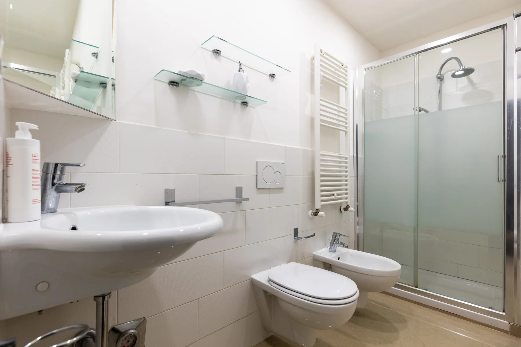 Un baño luminoso con azulejos, lavabo, inodoro, bidé y ducha de cristal.