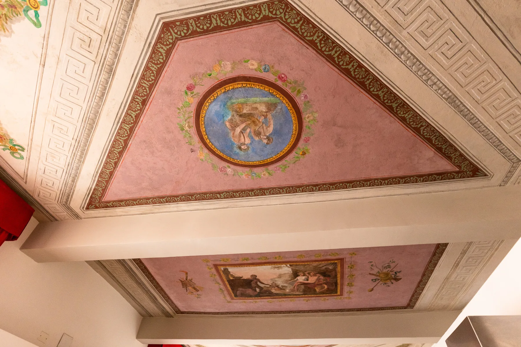 Un techo decorado presenta paneles rosados con medallones pintados ornamentados.