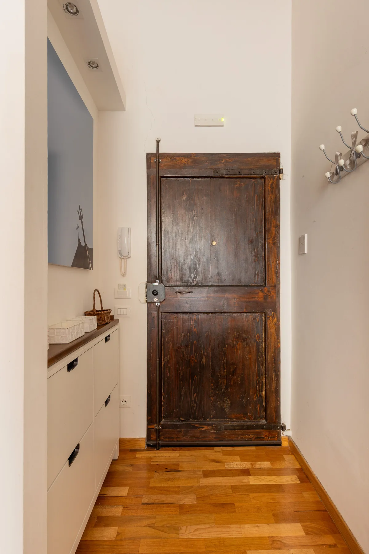 Un recibidor estrecho con una puerta de madera oscura y suelo de madera.