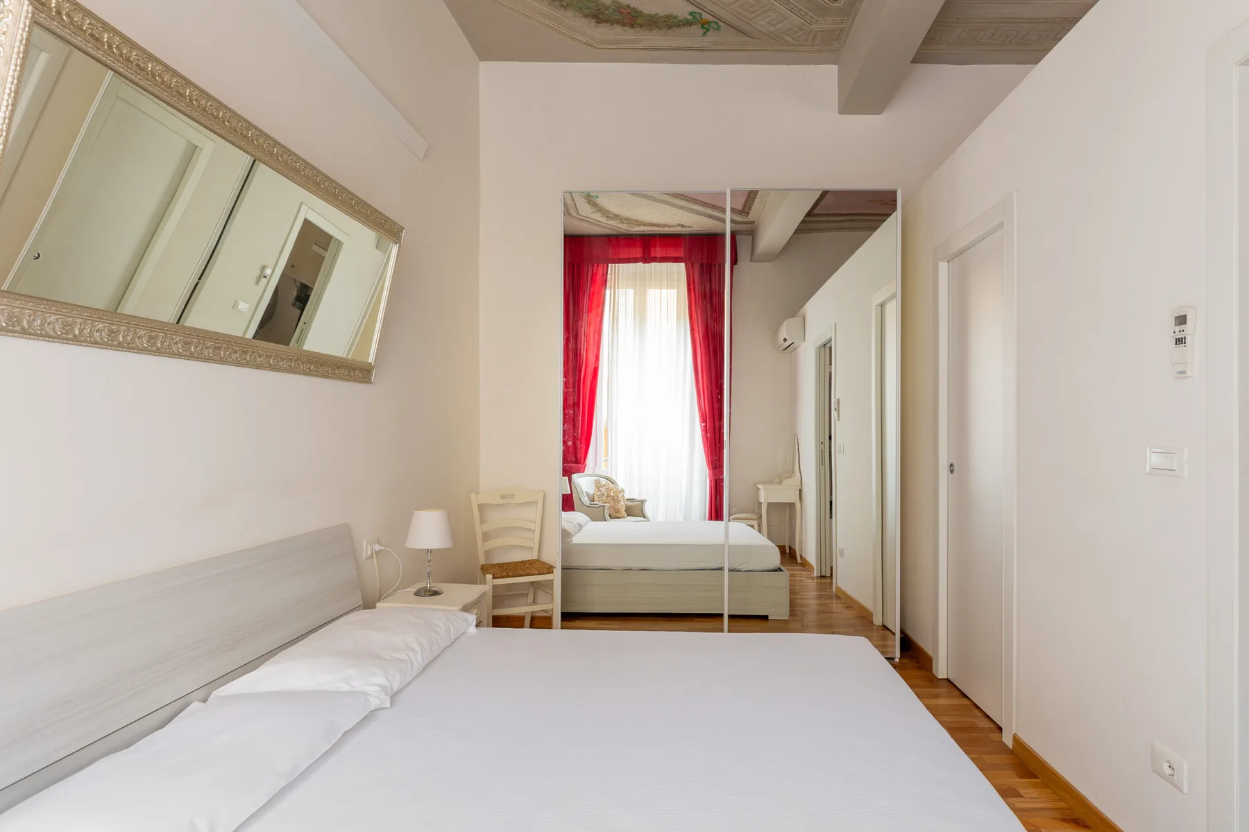 Un dormitorio luminoso con una cama, un armario con espejo y cortinas rojas.