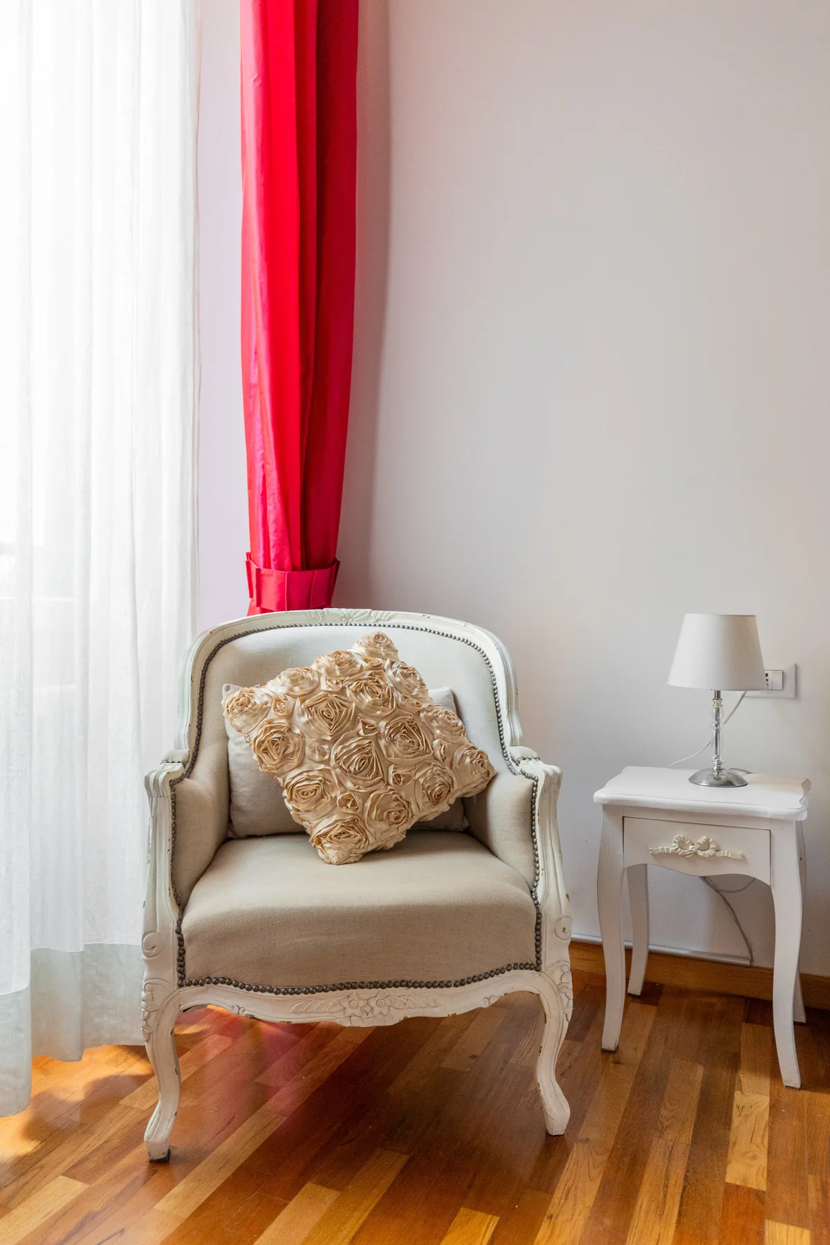 Un sillón claro con un cojín decorativo está junto a una mesita con lámpara.