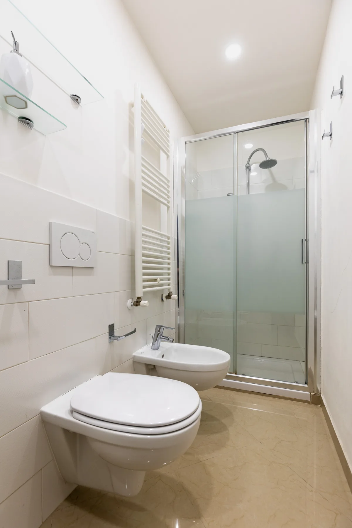 Un baño luminoso con inodoro, lavabo suspendido y ducha de vidrio.