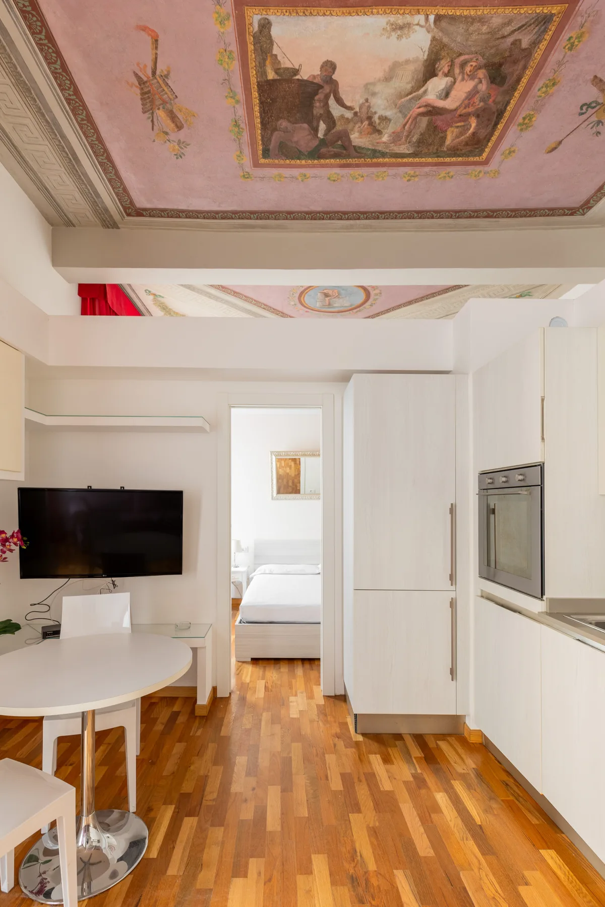 Una cocina y comedor luminosos se abren hacia un dormitorio, bajo un techo decorado.