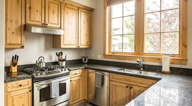 Una cocina con gabinetes de madera, encimeras oscuras y una ventana grande.