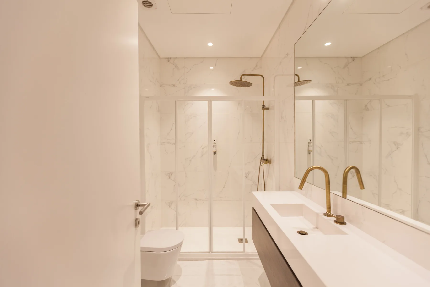 A bright bathroom with a glass shower and a long sink counter.
