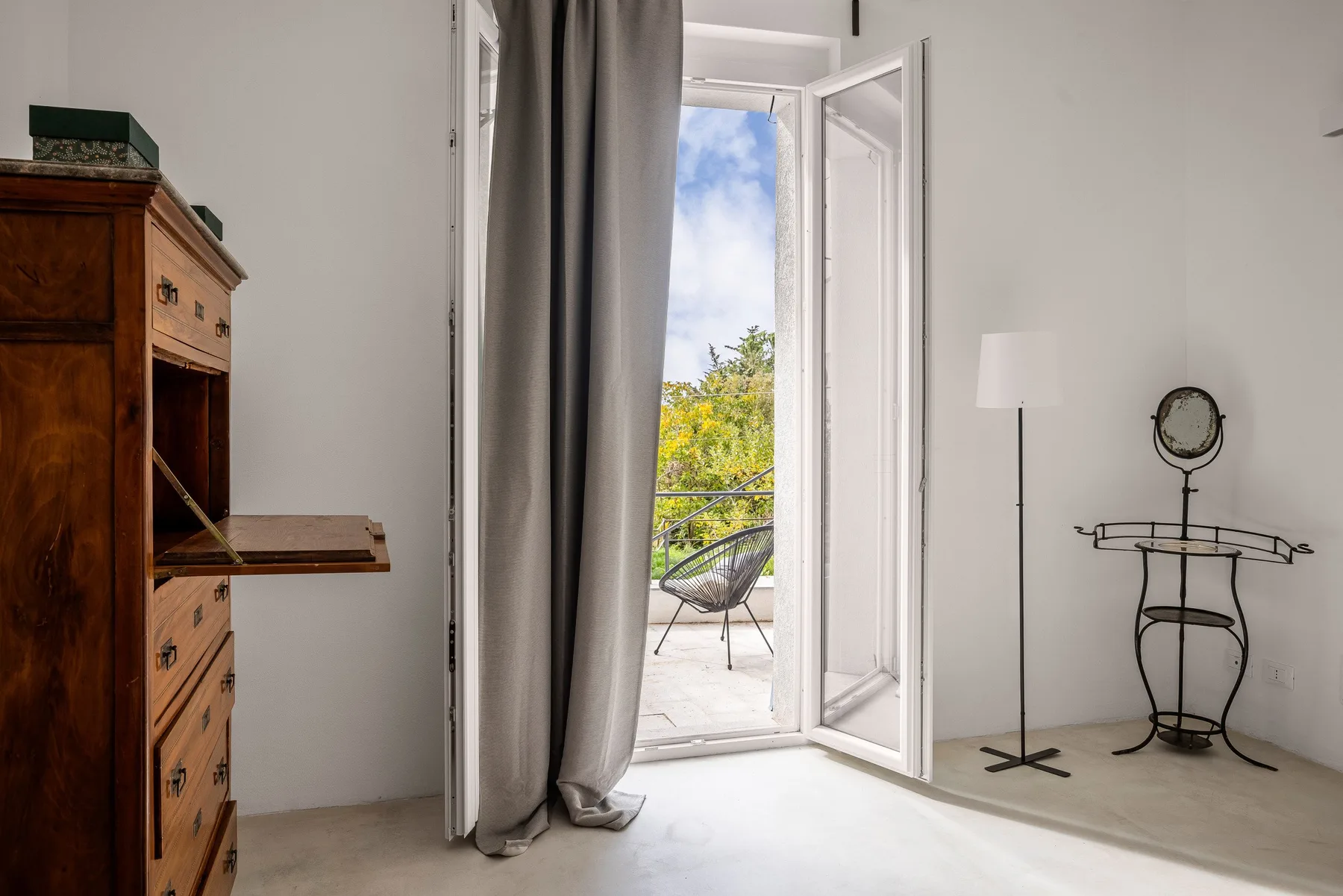 Una habitación luminosa da a un balcón a través de una puerta de cristal abierta.