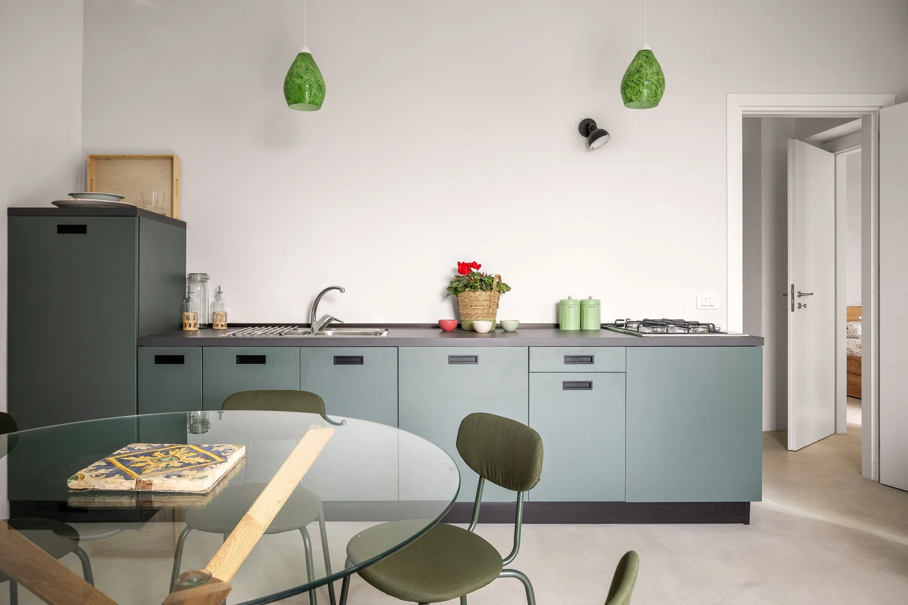 A modern kitchen with pale cabinets, a countertop, and a glass dining table.