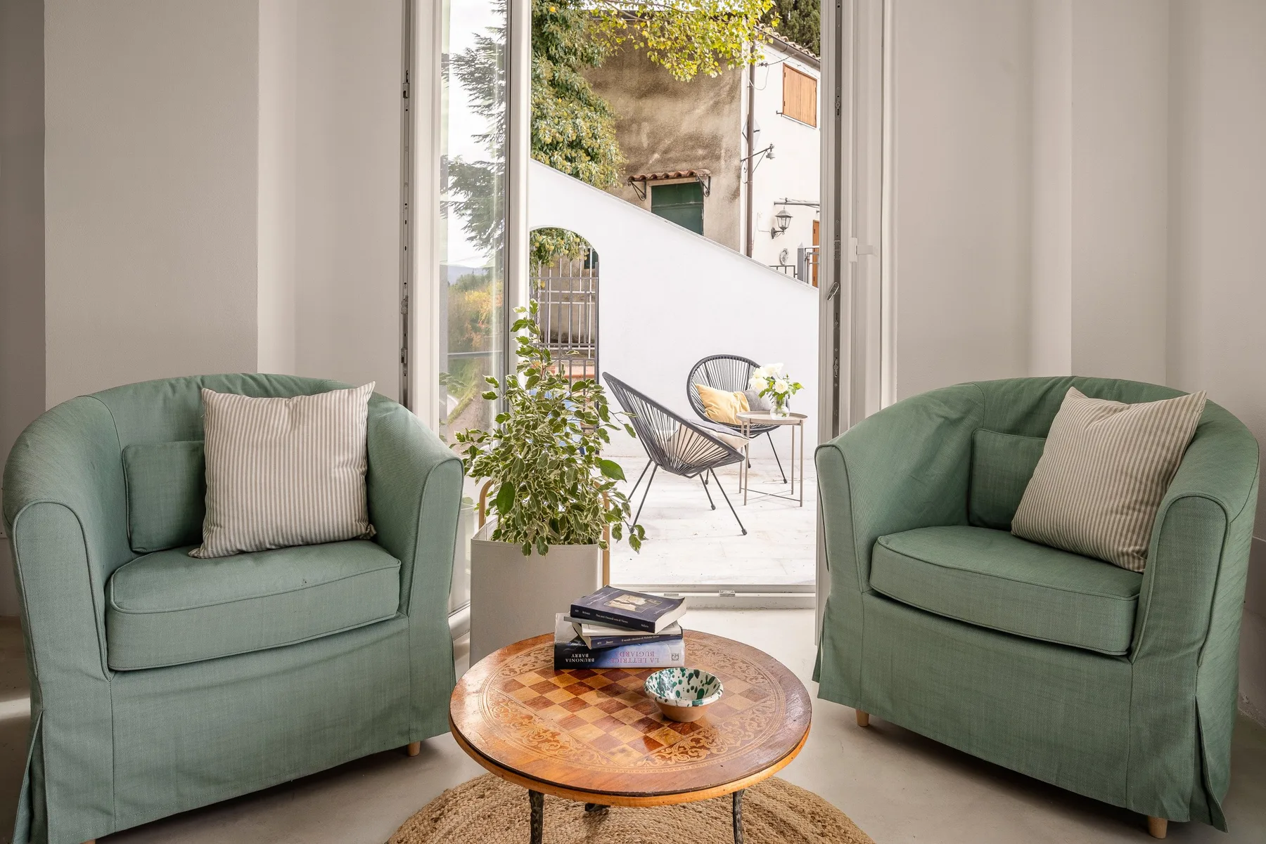 Una zona de estar con asientos verdes y una mesa redonda de madera junto a una ventana abierta.