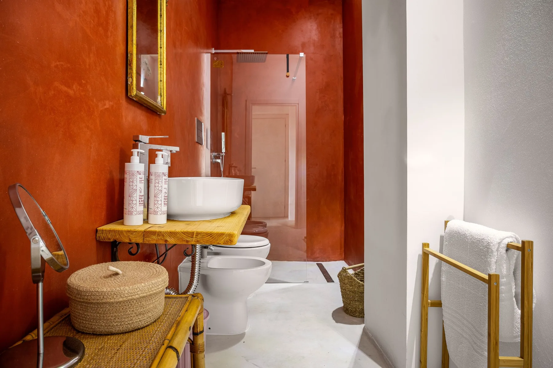 Un baño con lavabo e inodoro blancos junto a paredes rojizas.