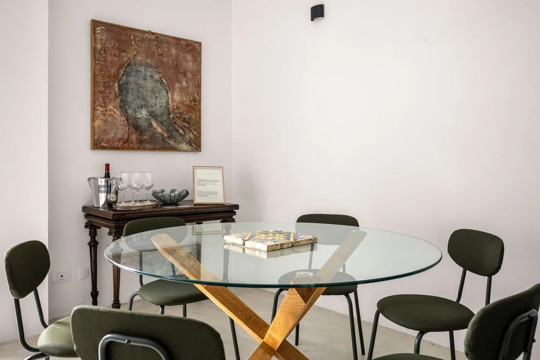 Un comedor con una mesa de vidrio y sillas oscuras bajo un cuadro.