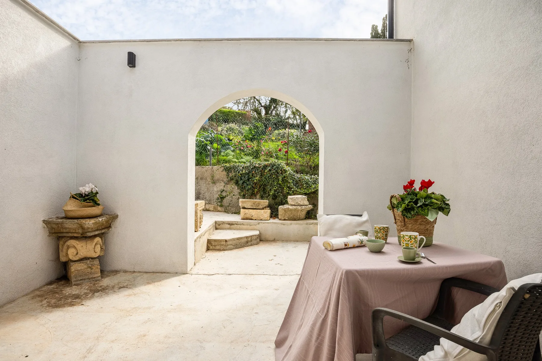 A sunlit courtyard with an arched opening onto a garden and a small table.
