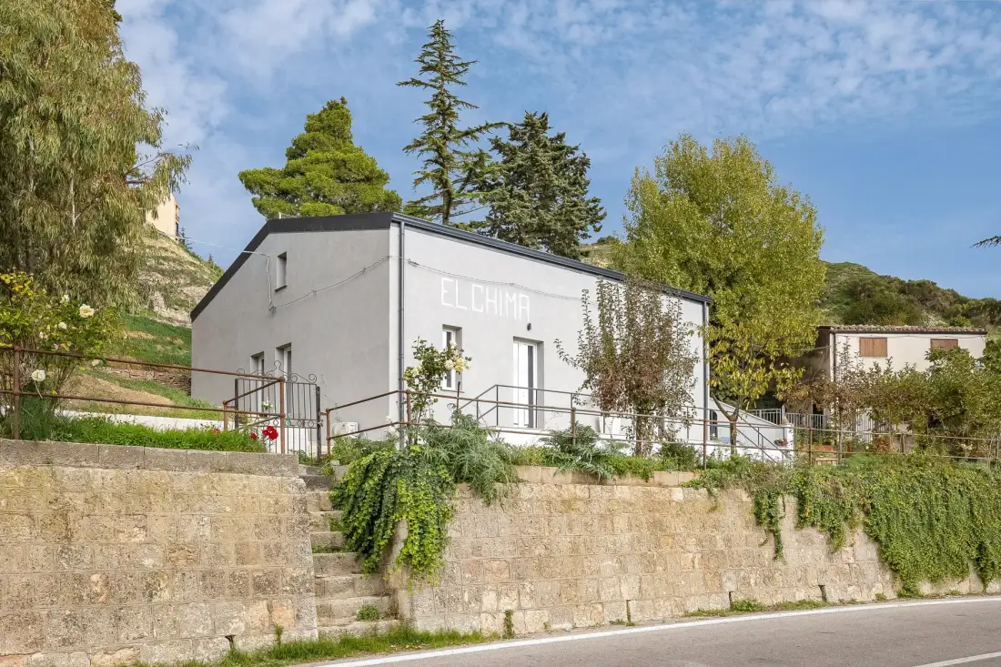 Un edificio blanco se alza sobre un muro de piedra, rodeado de árboles y vegetación.