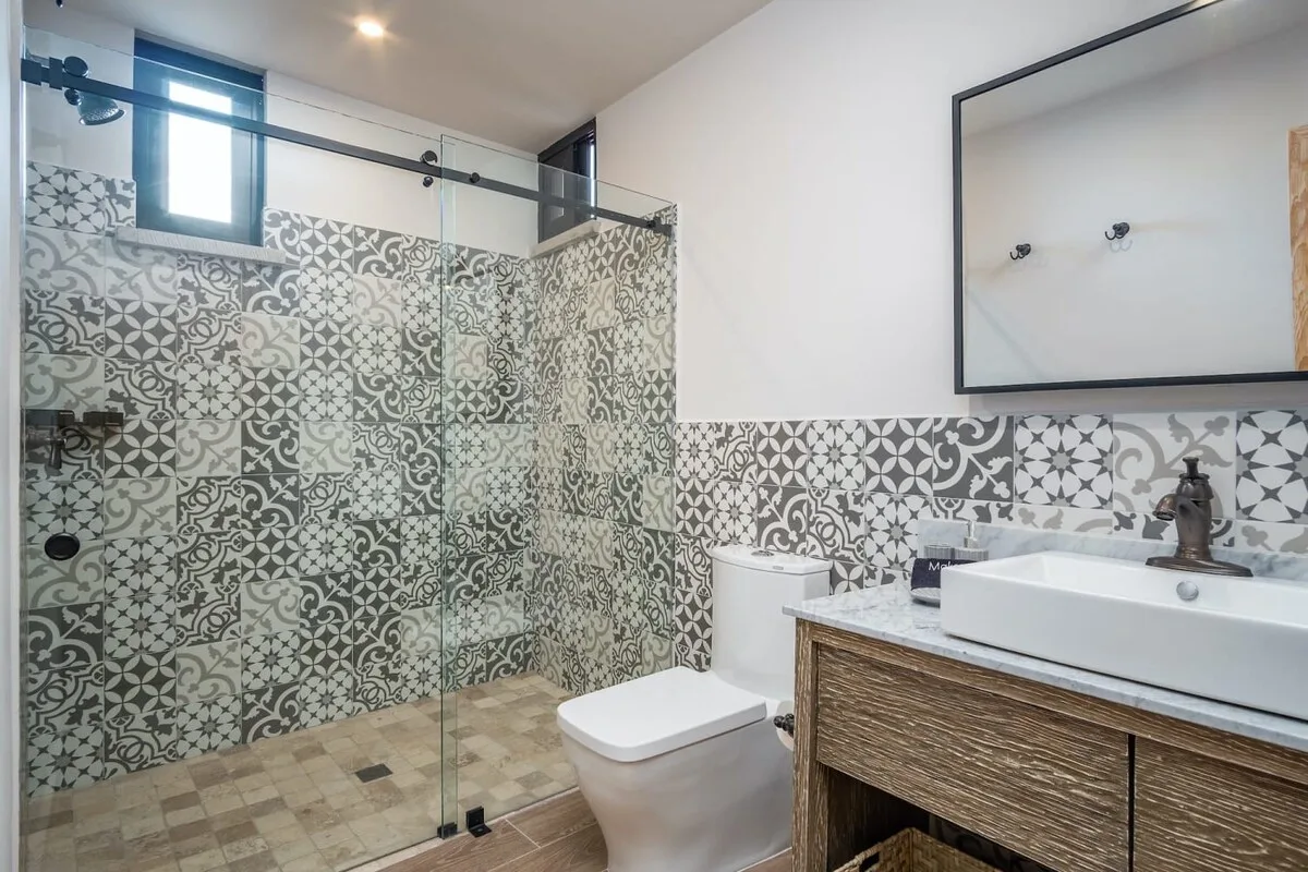 A patterned-tile bathroom with a glass shower, toilet, and sink.