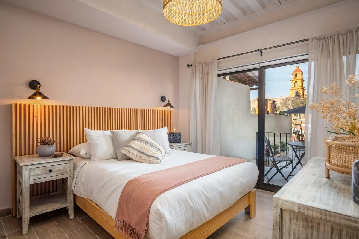 A bright bedroom with a bed beside an open balcony doorway.