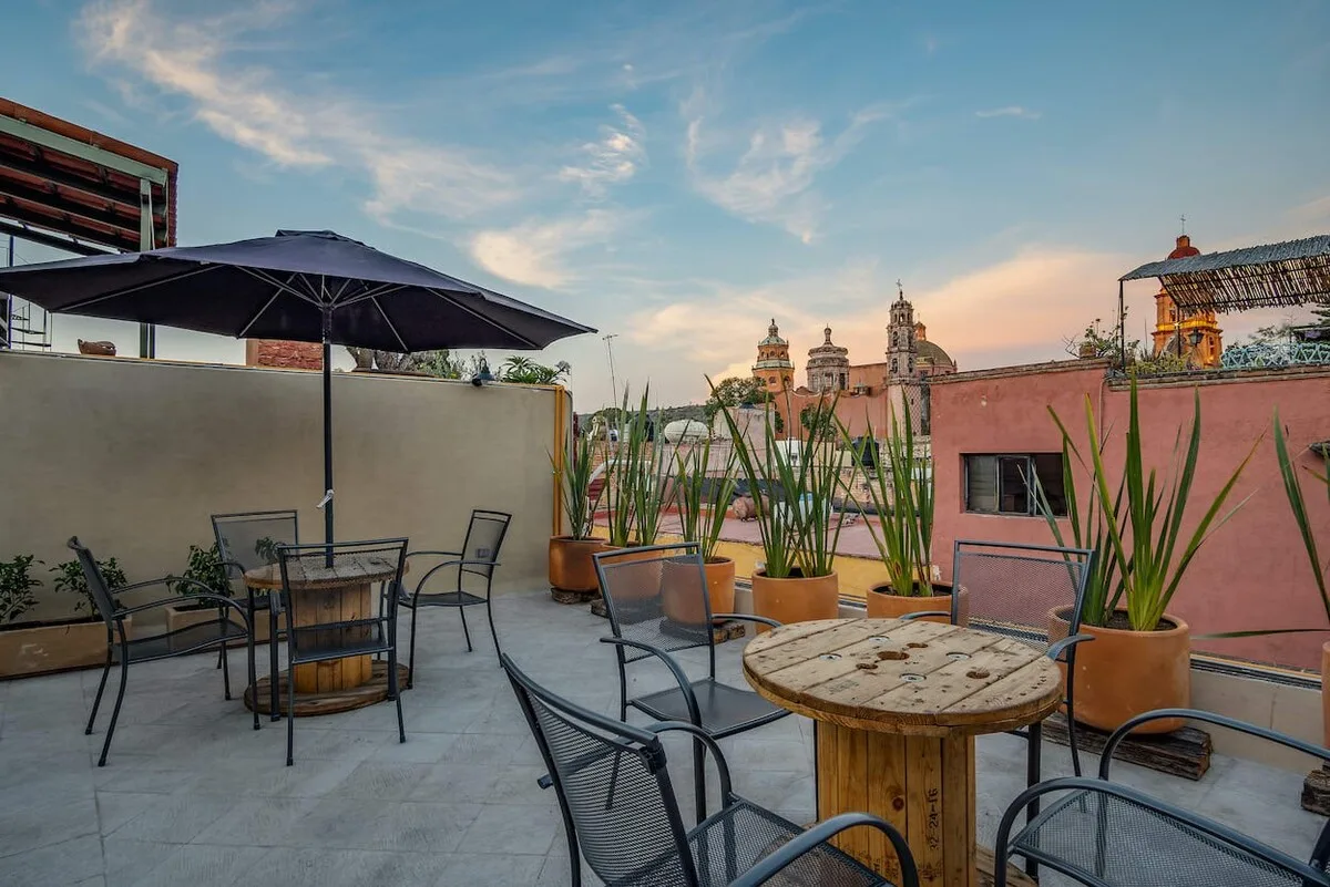 A rooftop terrace with outdoor seating, potted plants, and a view of nearby towers.