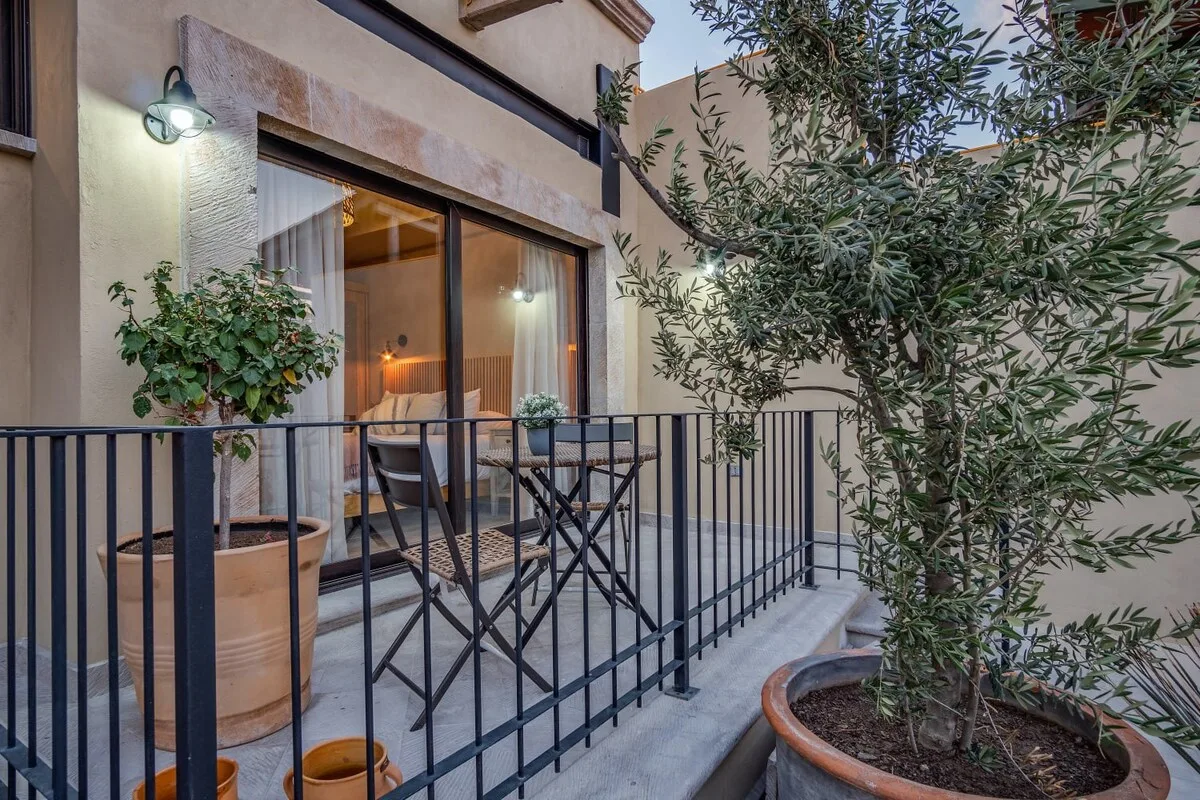 A small patio with metal seating overlooks a glazed door and potted greenery.