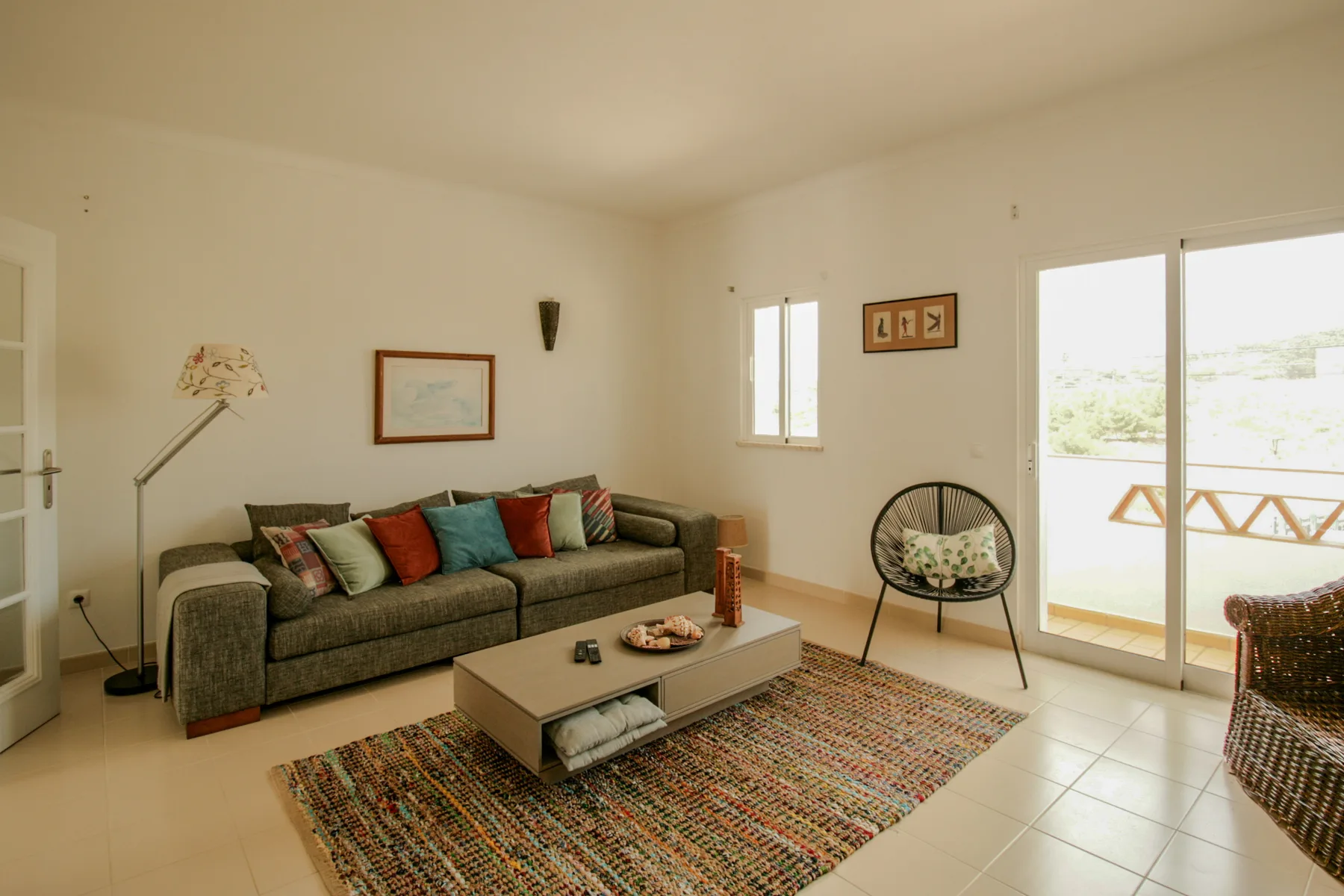 A bright living room with seating, a coffee table, and a glass door opening onto a terrace.