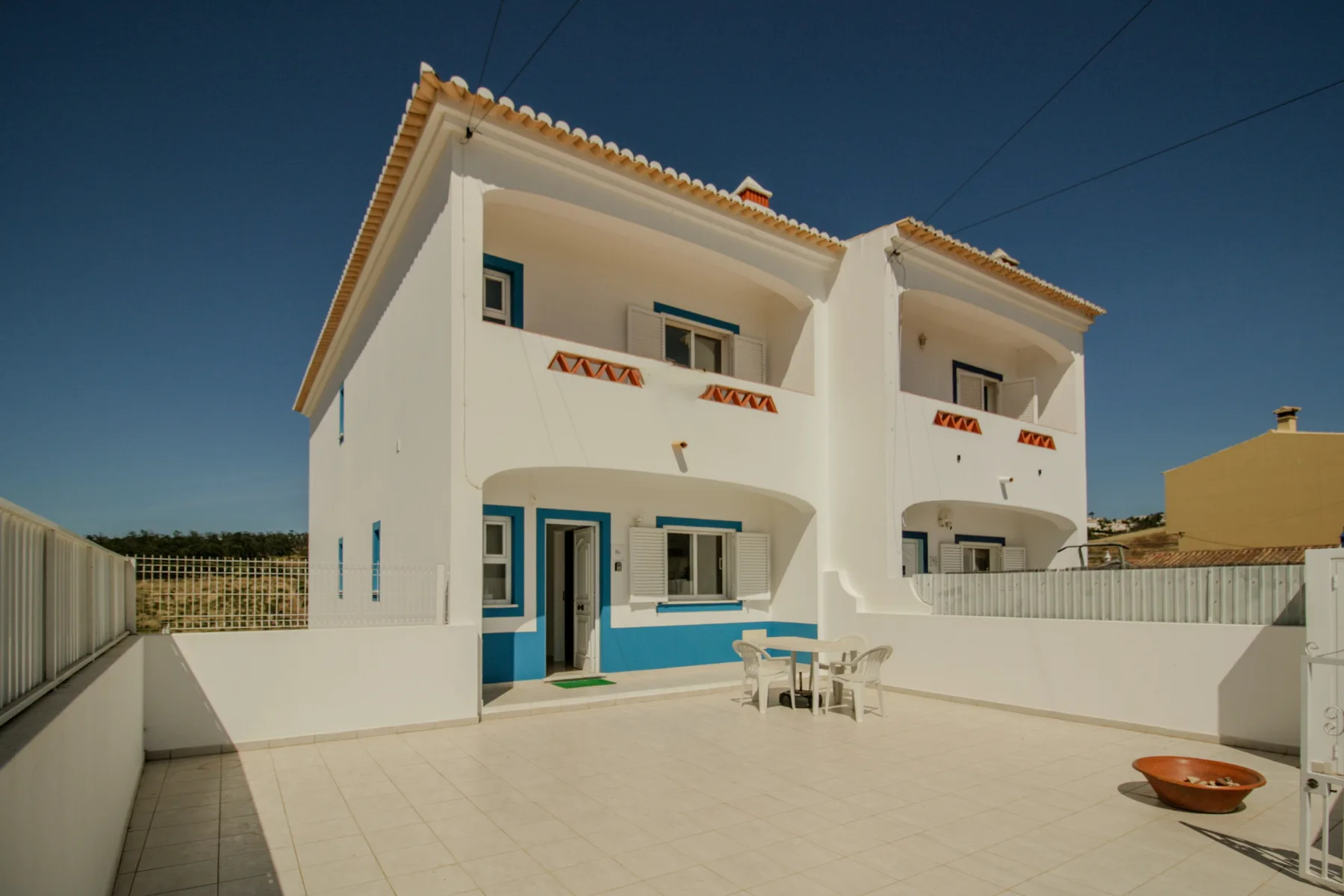 A white two-story house with blue trim faces a tiled outdoor courtyard.