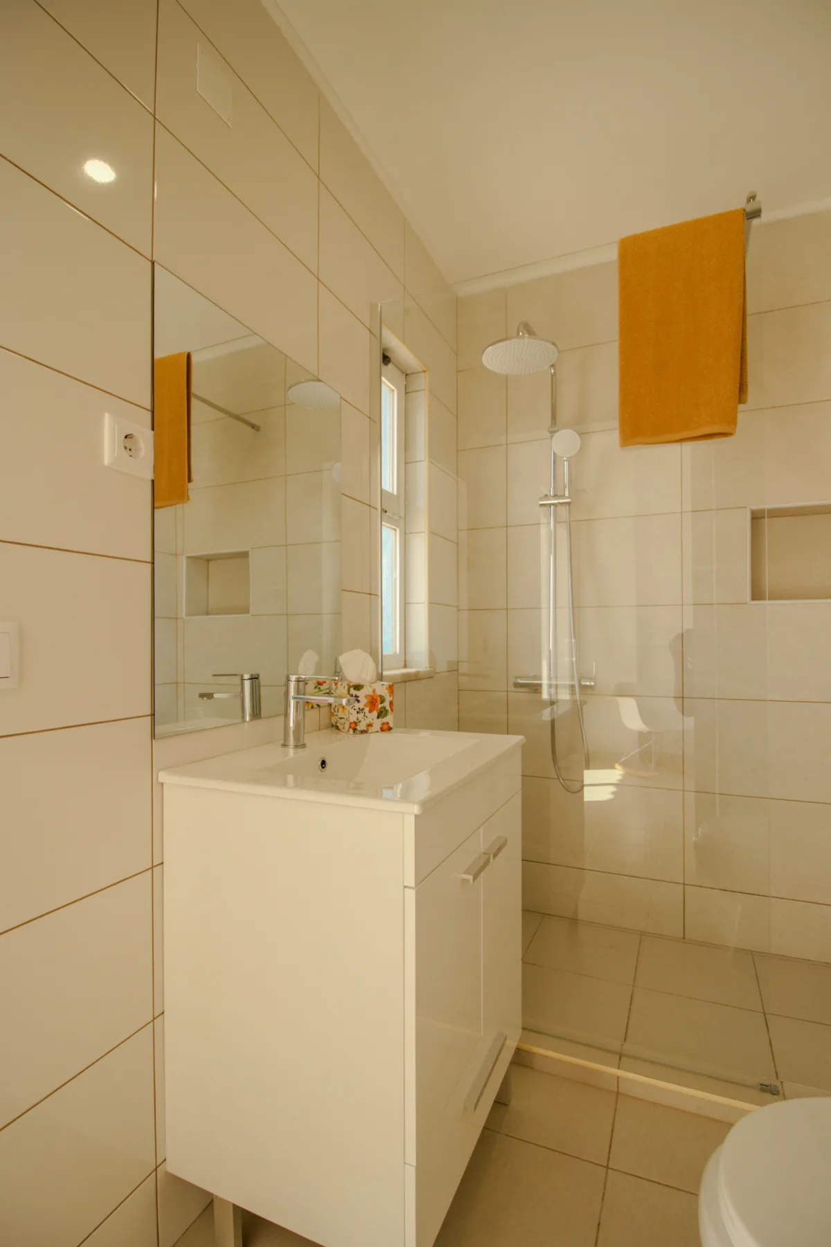 A tiled bathroom has a vanity sink beside a glass shower.