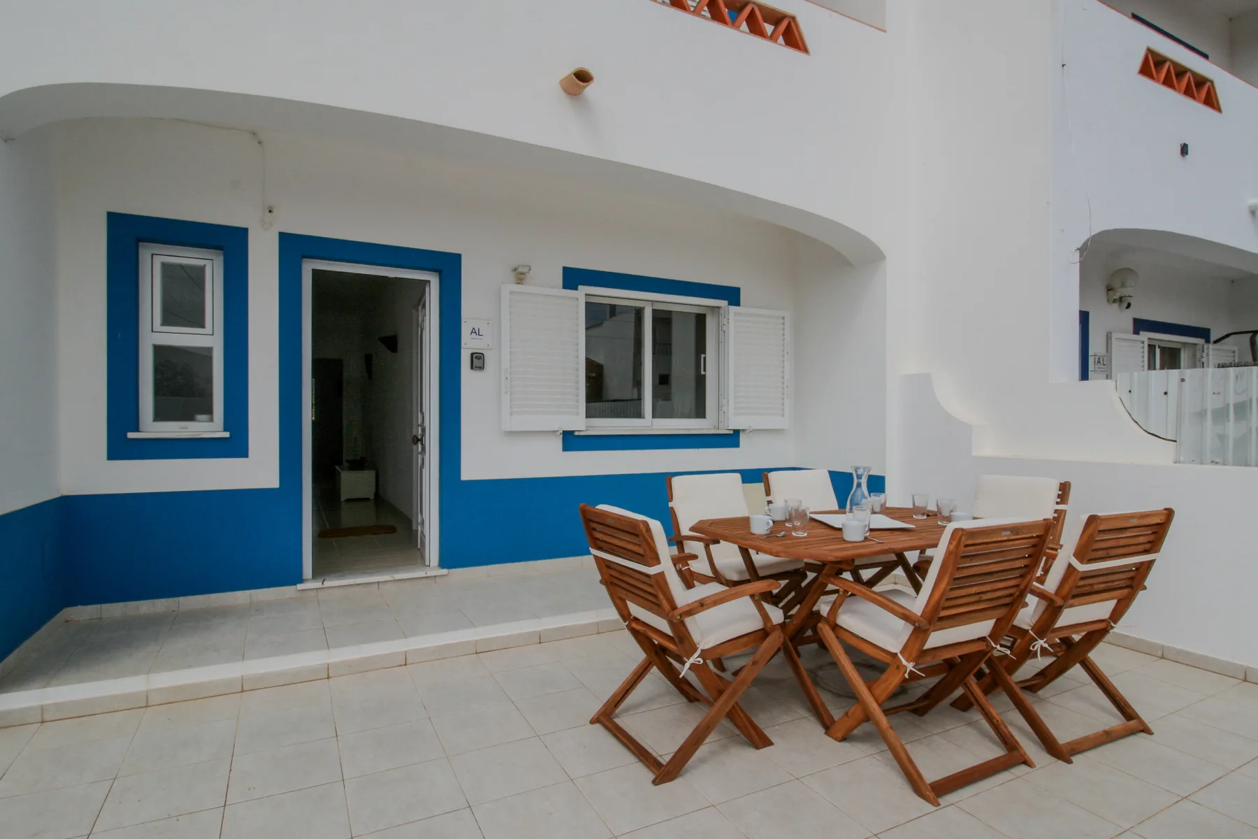 A tiled outdoor dining area sits beside a blue-and-white building facade.