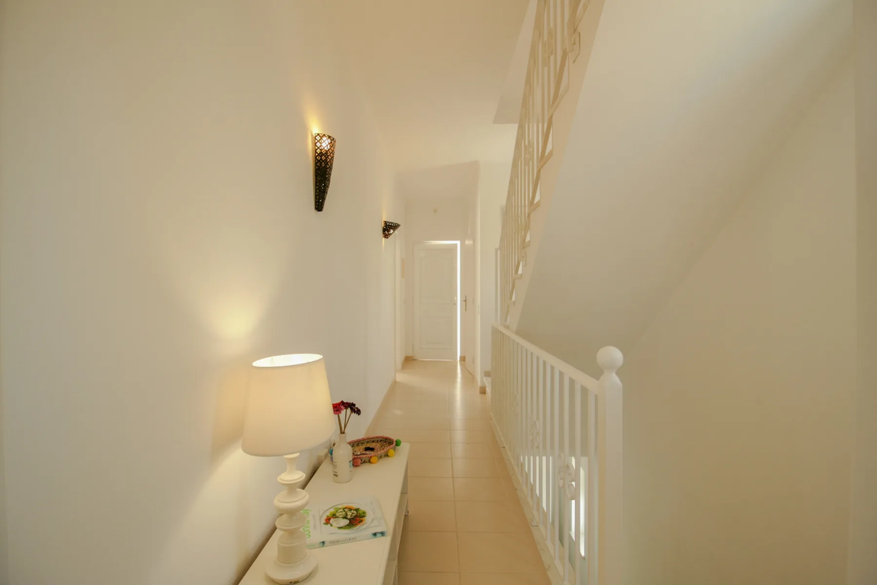 A narrow hallway with a staircase railing and a small console table.