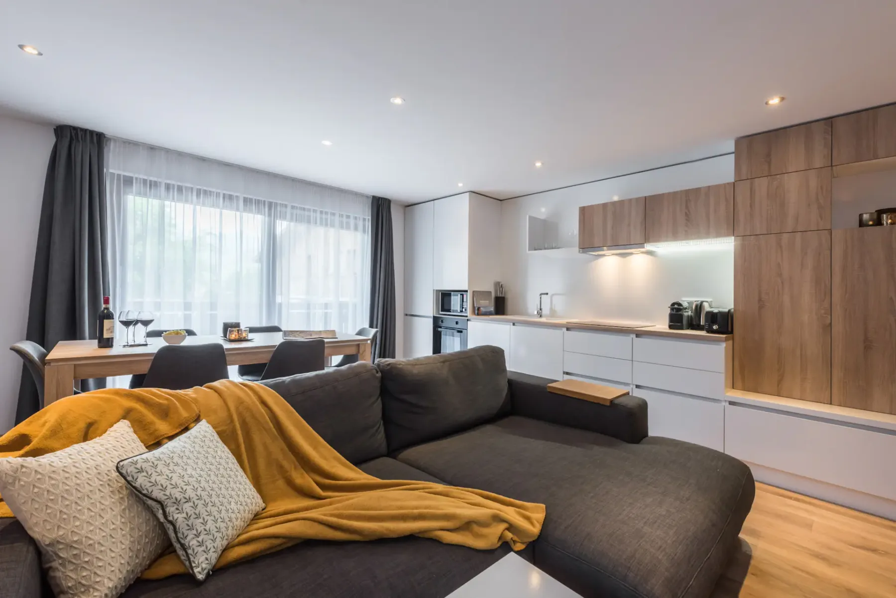 A living room opens onto a dining area and kitchen, with a large sectional sofa.