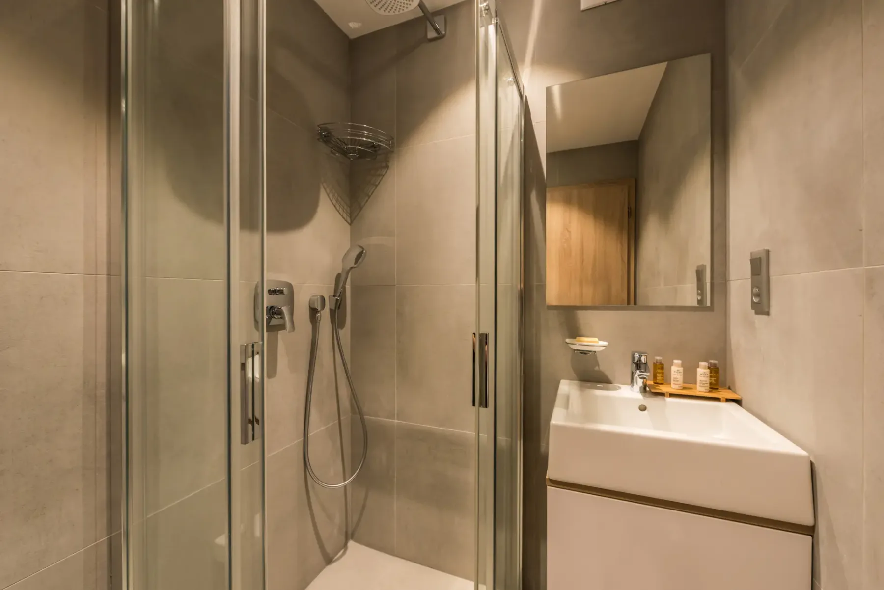 Un baño alicatado con una ducha de cristal y un lavabo bajo un espejo.