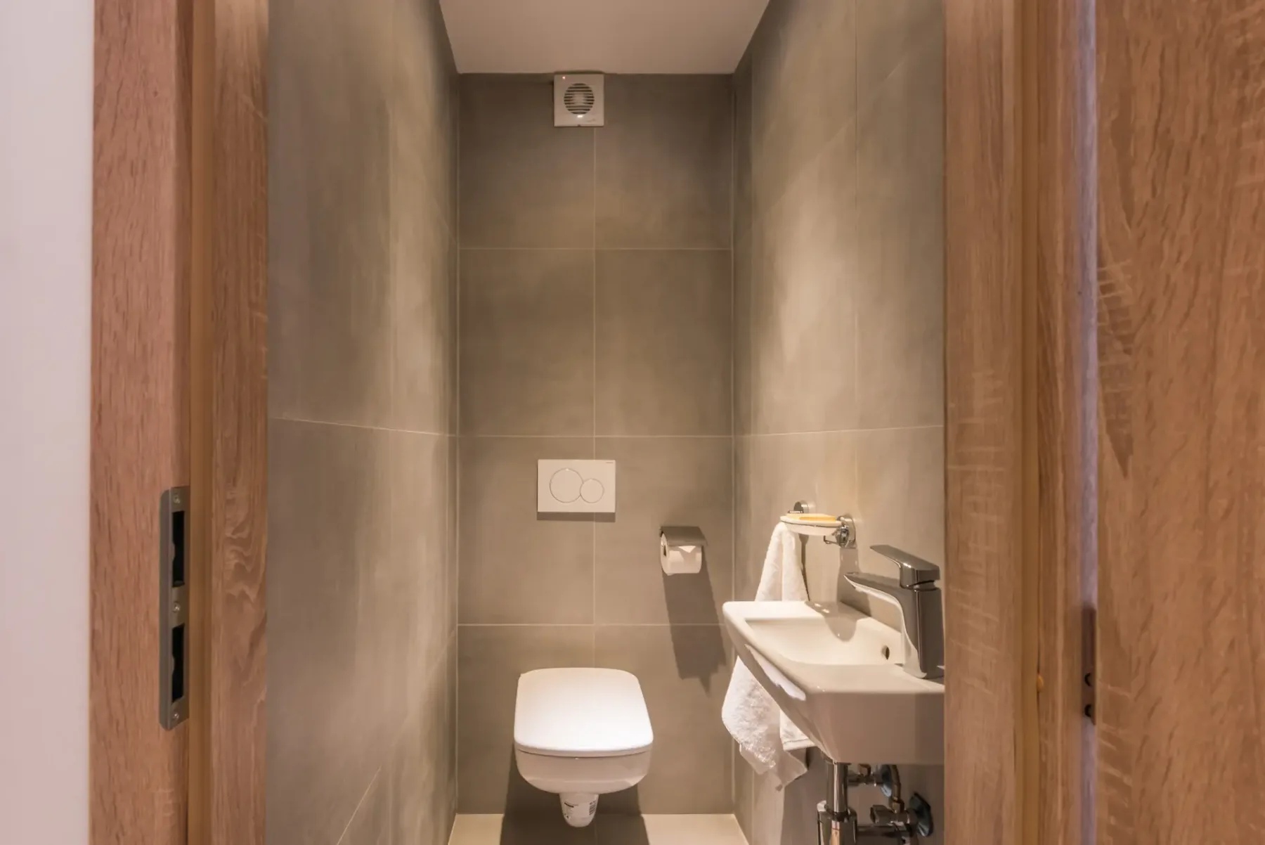 Un baño de azulejos grises con inodoro y lavabo suspendido.