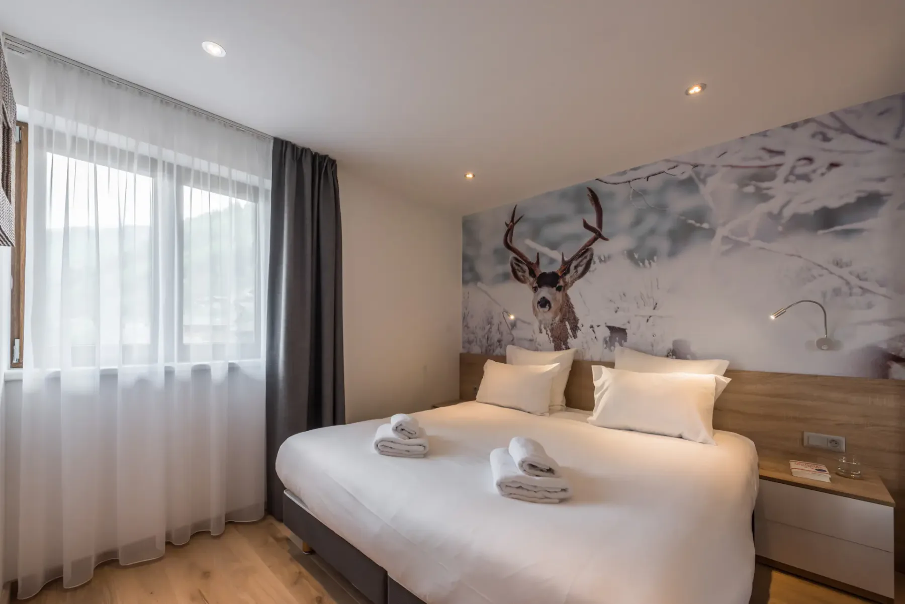 Un dormitorio con una cama bien hecha y un gran mural de un ciervo sobre el cabecero.