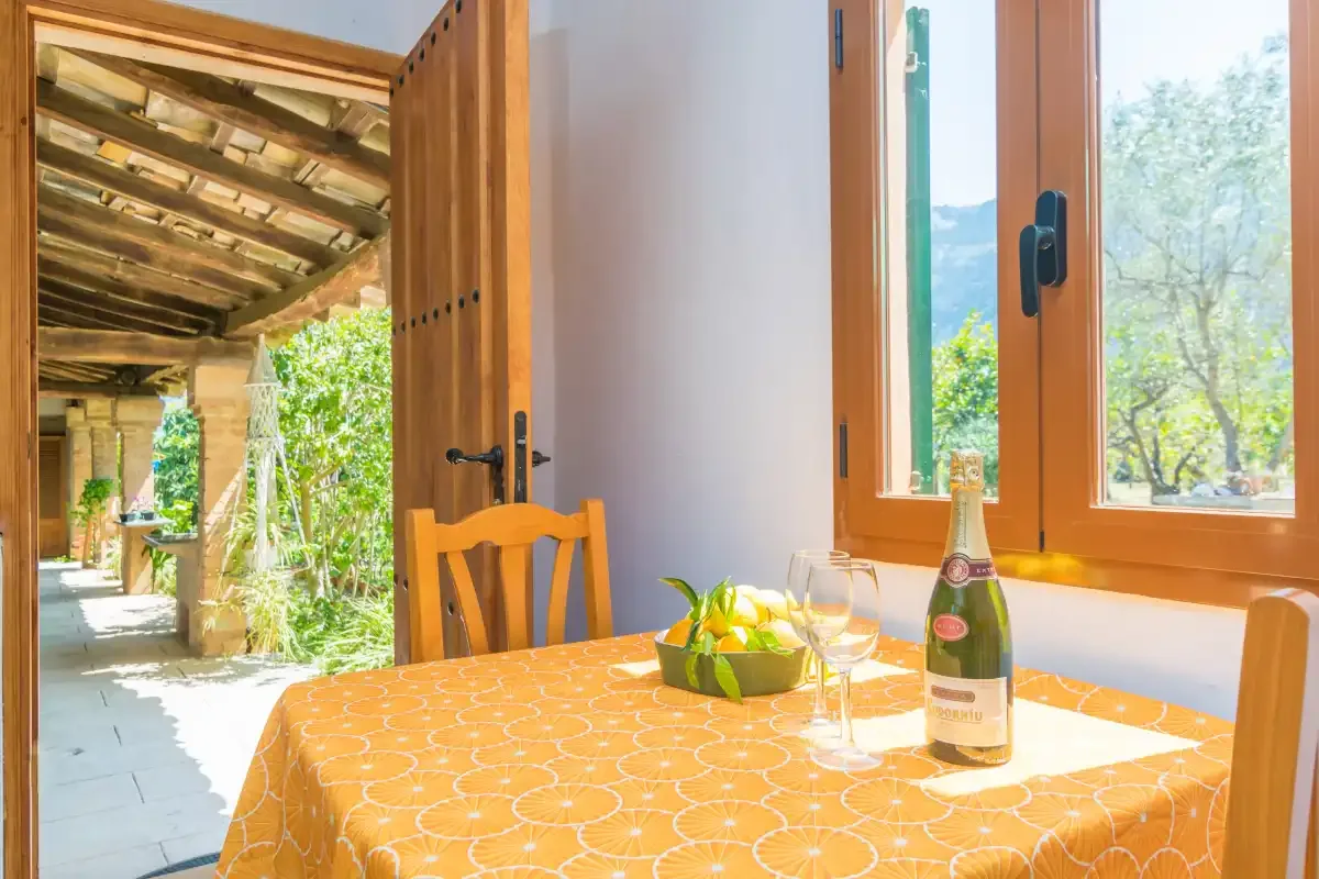 A dining table with a patterned cloth sits beside open wooden doors and windows.