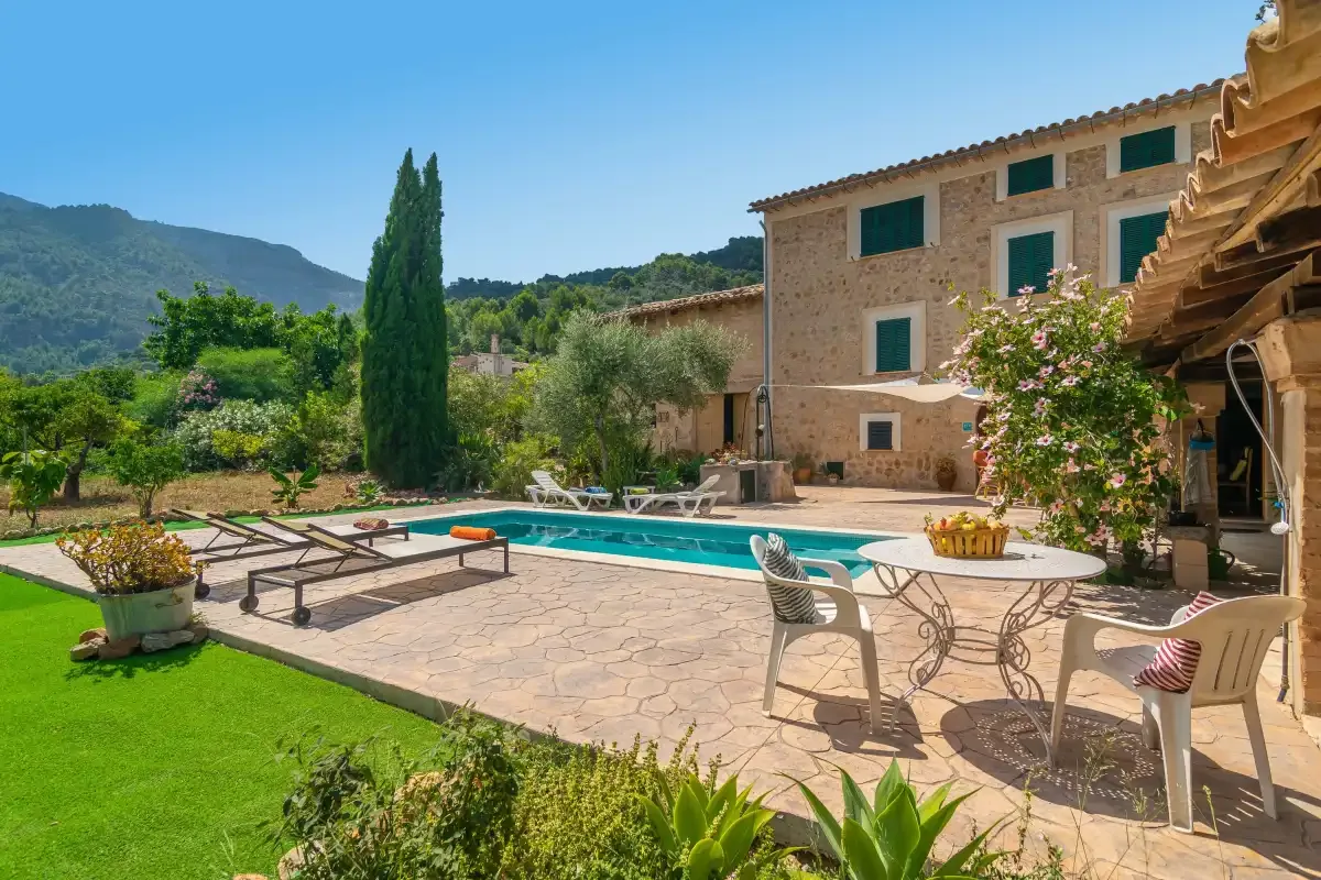 A swimming pool and patio with outdoor seating beside a stone house.