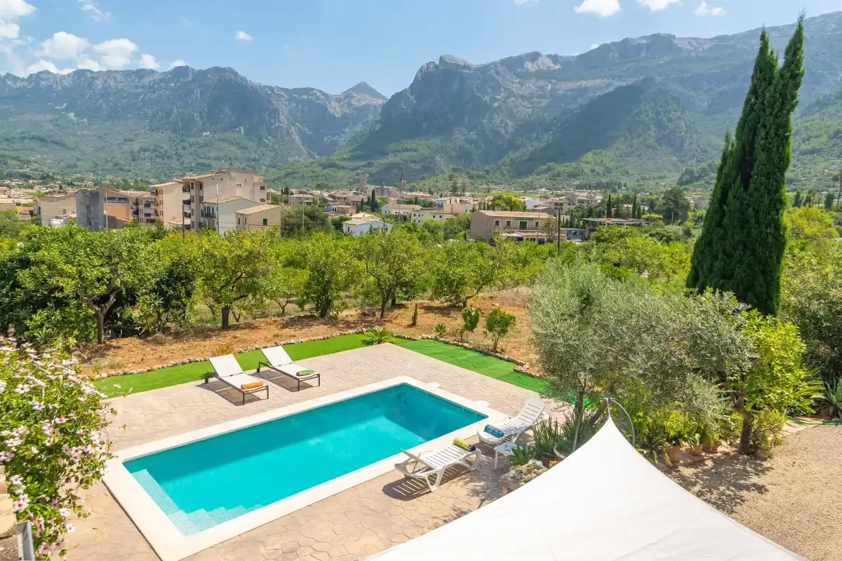 A swimming pool and sun loungers overlook a green valley and mountains.