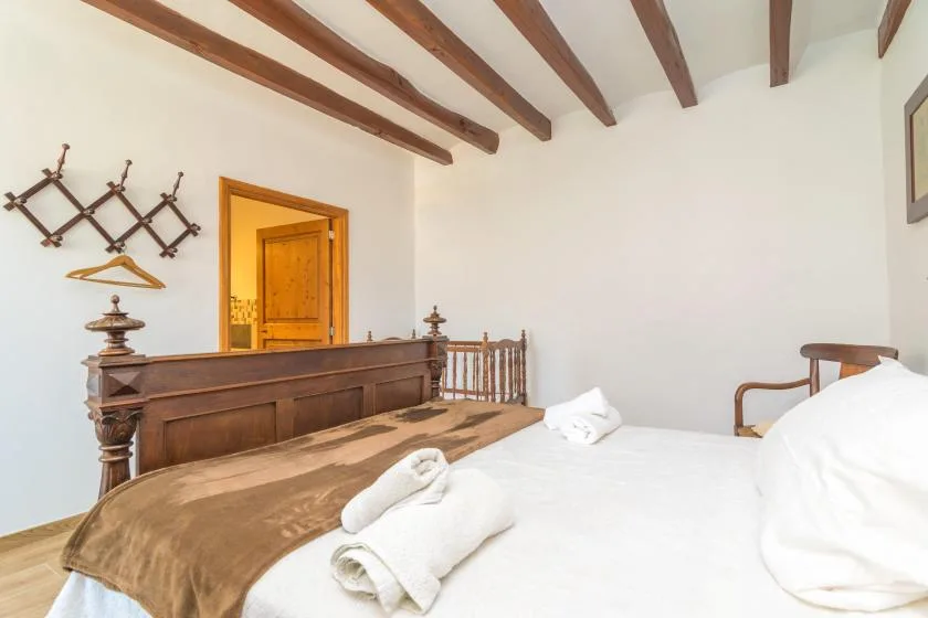 A bedroom with a white bed and dark wooden ceiling beams.