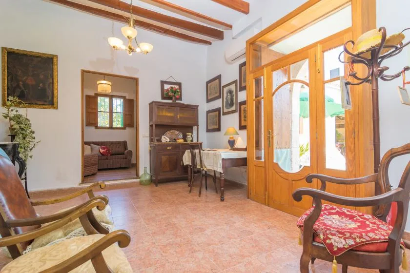 A living room with wooden seating, framed artwork, and a bright glass-paneled doorway.