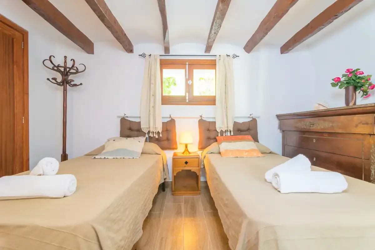 A bedroom with two beds, a central nightstand, and exposed ceiling beams.