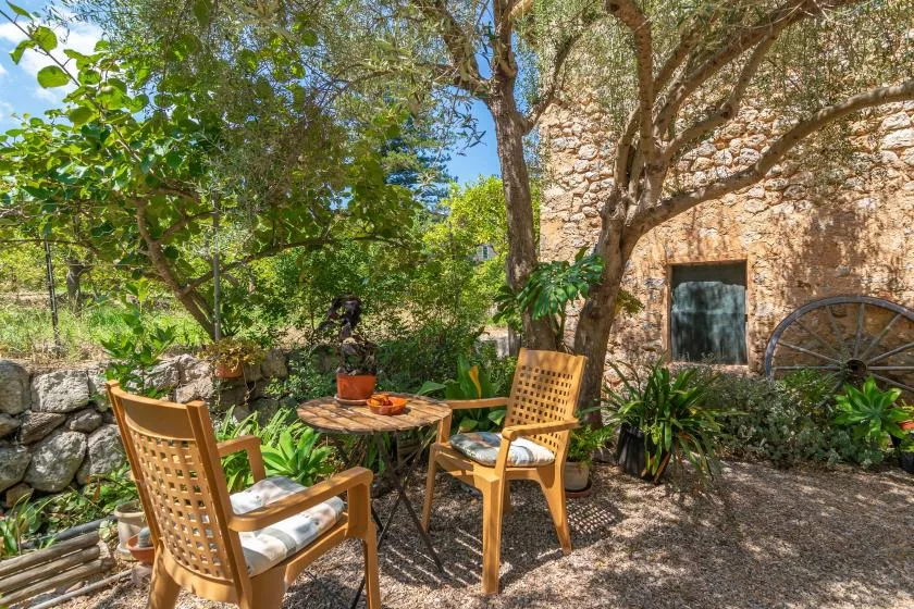 A garden seating area beside a stone wall, shaded by leafy trees.