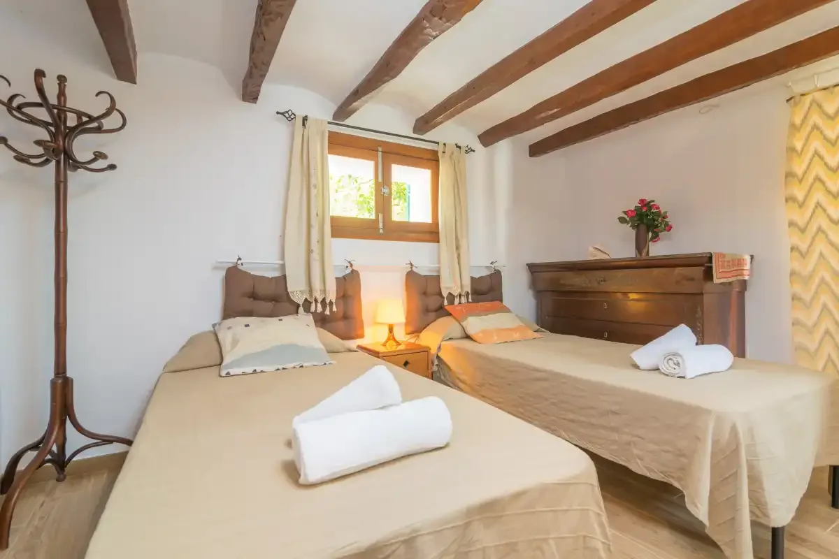 A bedroom with two beds, a wooden chest, and exposed ceiling beams.